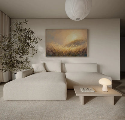 Framed painting of a wooden cross on a sunlit golden wheat hillside at sunrise displayed in a neutral minimalist living room
