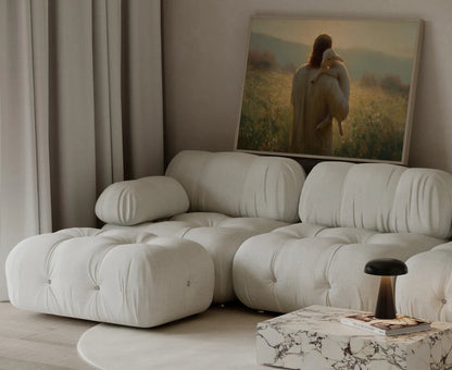 Jesus carrying a white lamb through a golden wildflower field at sunrise intimate close-up art print above a sofa in a warm neutral living room – JesusArtworks
