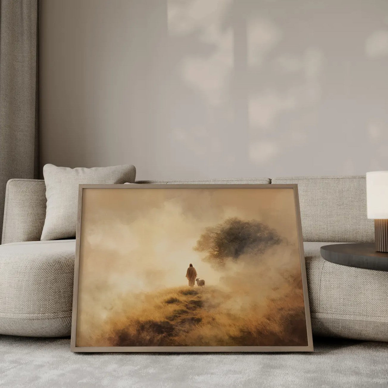 The Shepherd's Path Jesus walking with a lamb wall art print in a gold frame leaning against a modern beige sofa – Christian home decor by JesusArtworks